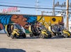 Three yellow GoCars with tourists in them lined up in front of a brightly colored mural on a sunny day in Las Vegas.