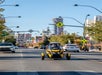 A yellow GoCar driving down the Las Vegas strip with cars around it and the city in the background on a sunny day.