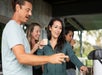 A group of four adults stand together outdoors, talking and smiling while holding drinks.