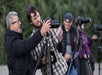 Two men adjust a camera on a tripod while others focus on their own equipment in the background.