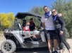 Two young boys sitting in a silver ATV with their parents standing at the front, all smiling, on a sunny day with Desert Dog Off Road Adventures.