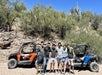 A group of six adults standing in front of a red and a blue ATV with the rocky desert behind them on a sunny day.