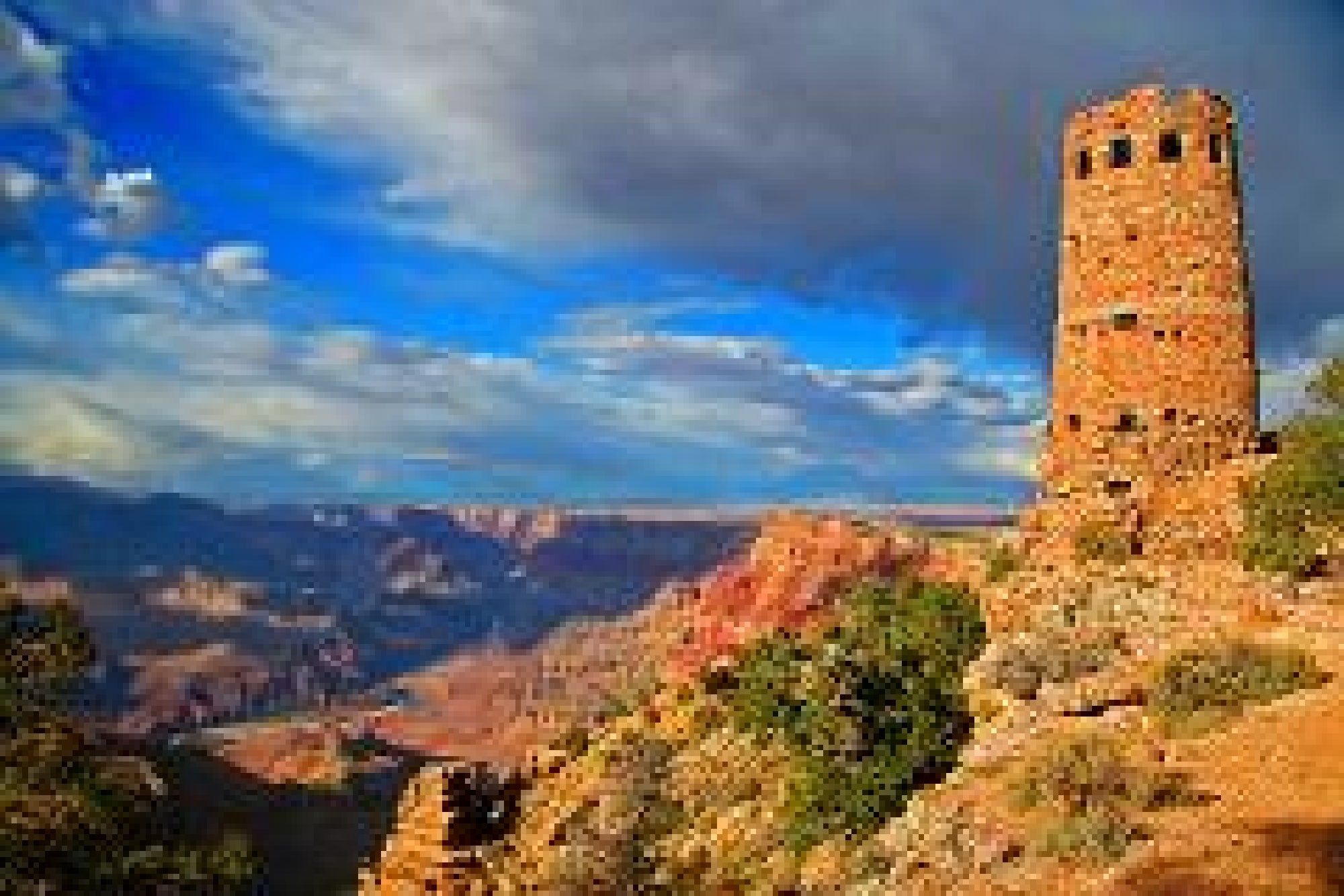 A stone watchtower stands on the edge of a canyon under a partly cloudy sky, overlooking the vast landscape of the Grand Canyon.