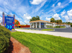 Motel exterior with a "Developer Inn & Suites" sign. Building features two stories, palm trees, and adjacent parking lot. Blue sky with clouds overhead.