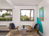 Two modern chairs and a small table with a plant in a bright room, featuring two windows and a colorful wall art piece.