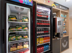 A vending area with two refrigerators: one with frozen meals and pizzas, the other stocked with various sodas and drinks. A coffee machine is on the right.