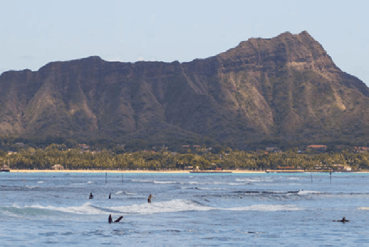 Wide shot of the Diamond Head cone seen from the coast off Waikiki with surfers in the lights blue water on a sunny day.