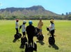 A group of people wearing helmets stand on Segways in a grassy field, with a guide giving instructions; a large mountain is visible in the background.