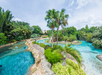 A winding lazy river surrounded by lush greenery and palm trees, with people floating on inner tubes in clear blue water.