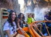 A group of young people laugh and get splashed with water while riding a theme park water ride.