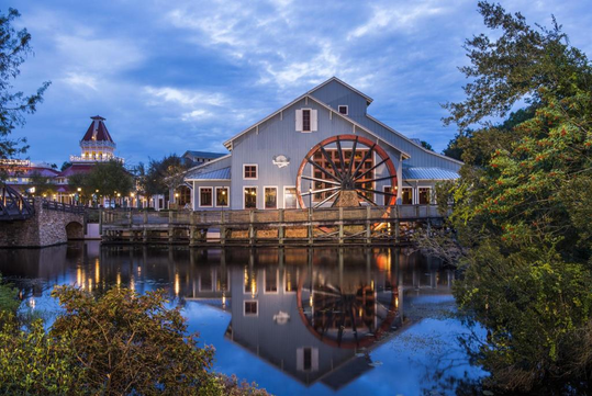 Exterior view of the resort, the boardwalk, a red waterwheel mill, and the river.