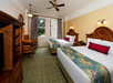 2 Queen beds and a wooden table and chairs inside a guest room.