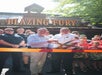 Two men cut a ceremonial ribbon in front of a crowd at the entrance of an attraction called "Blazing Fury.