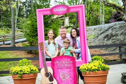 A family posing in a pink photo frame at the entrance to Dollywood Theme Park in Pigeon Forge, TN