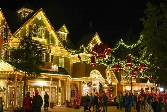 People walk past a festive building adorned with numerous Christmas lights at night.