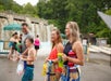 Group of people in swimsuits holding towels and cups, walking in a water park area with waterfalls in the background.