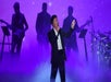 Donny Osmond in a black suit and white shirt singing on the stage with fog and a band behind him at Harrah’s in Las Vegas.