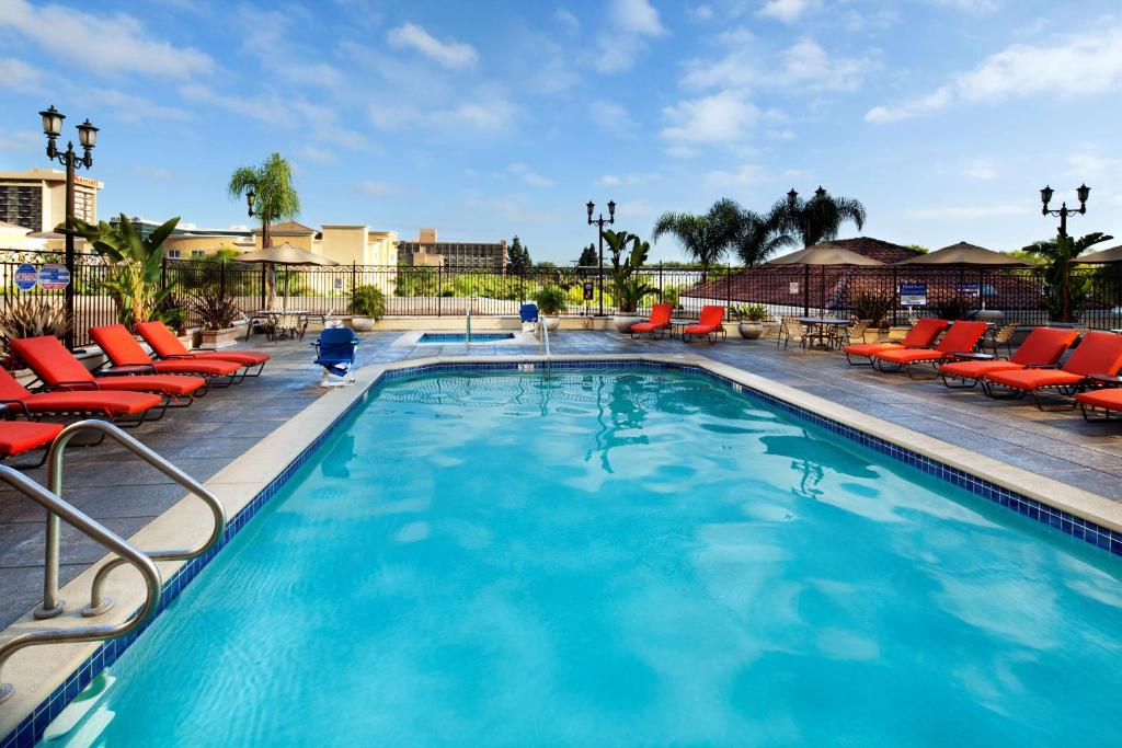Outdoor pool with clear blue water, surrounded by red lounge chairs and palm trees, under a blue sky.