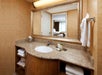 A hotel bathroom with a granite countertop, sink, mirror, and towels. A bed and window are reflected in the mirror.