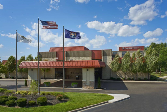 Hotel building with a red roof, surrounded by trees and flags, including the American flag, flying in front. The sky is partly cloudy.