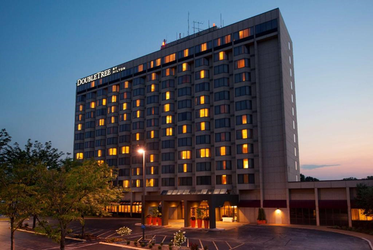 Exterior view of a multi-story hotel building at dusk with lit windows and a sign reading "DoubleTree by Hilton" on the top corner.