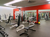 A gym with various exercise machines, benches, and mirrors. The walls are painted red and white.