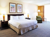 A hotel room with a large bed, two lamps, framed artwork, an armchair, and a window with curtains.