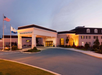 Front view of a resort building with an arched entrance. U.S. and state flags are on flagpoles to the left. Illuminated at dusk with a curving driveway and landscaped shrubs.