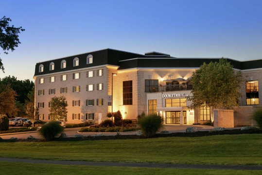 Exterior of a multi-story DoubleTree hotel at dusk, with warm lights illuminating the entrance and surrounding greenery.