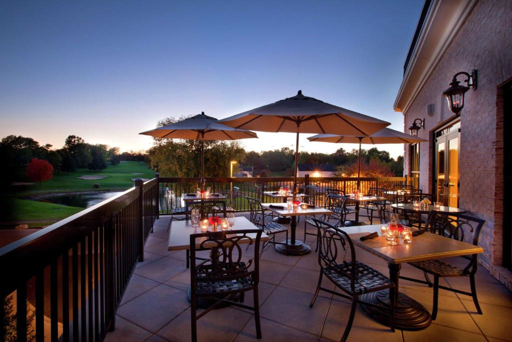 Outdoor terrace with tables and chairs under umbrellas at sunset. Lit candles are on the tables, overlooking a golf course and trees.