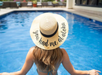Woman in a sunhat with "You had me at aloha" written on it sits at the edge of a swimming pool with her feet in the water.