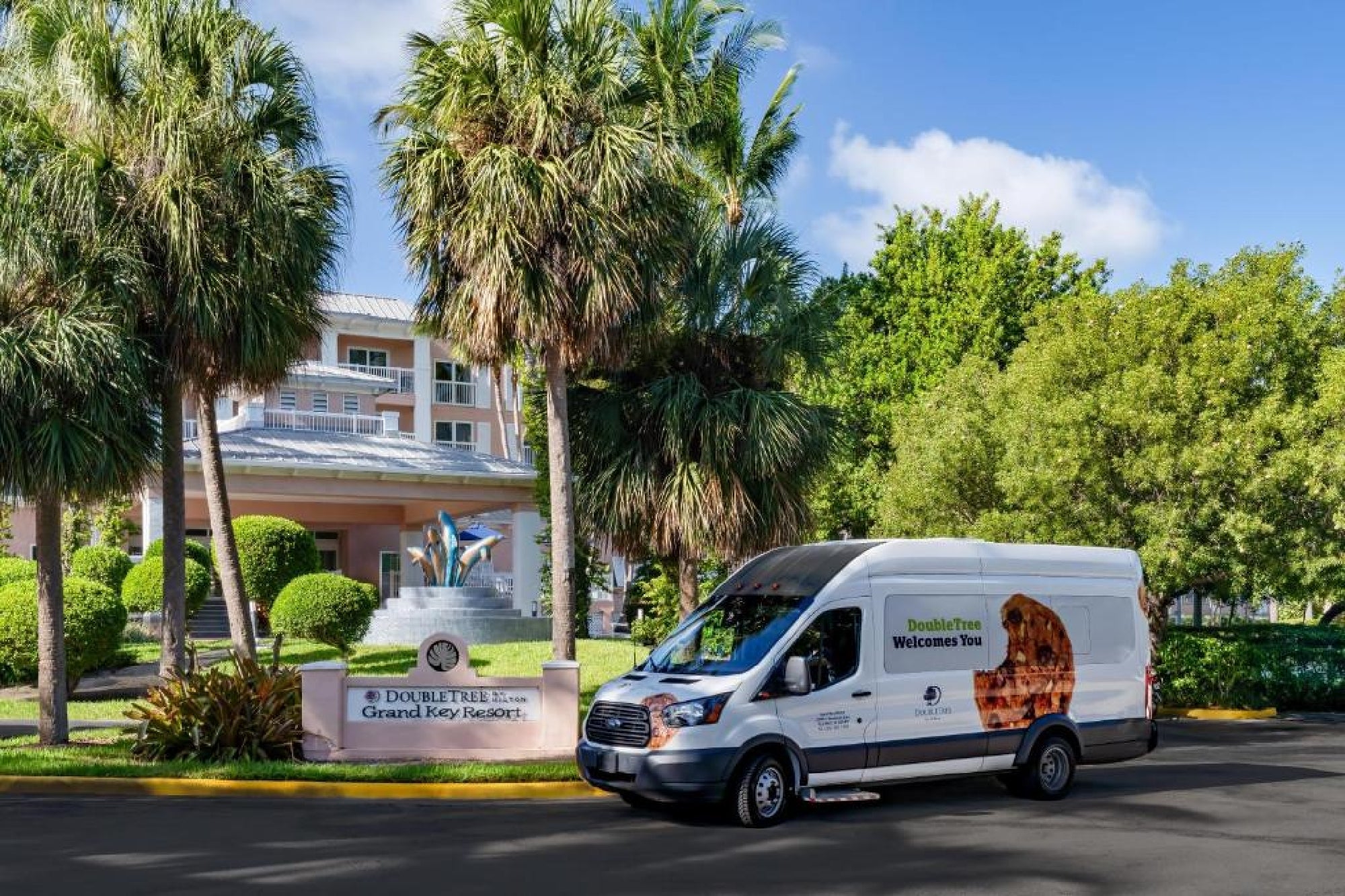 A white DoubleTree van is parked in front of a hotel entrance with palm trees, landscaping, and a sign reading "DoubleTree Resort Grand Key Resort.