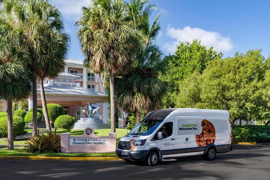 A white DoubleTree van is parked in front of a hotel entrance with palm trees, landscaping, and a sign reading "DoubleTree Resort Grand Key Resort.