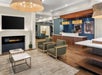 Modern hotel lobby with a fireplace, seating area with two armchairs and tables, and a reception counter with computers.