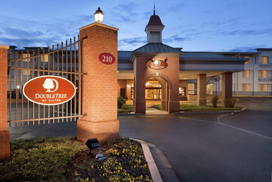 Entrance to a DoubleTree by Hilton hotel with a well-lit sign, brick pillars, and a circular driveway at dusk.