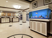 Hotel lobby with a large fish tank to the right and a reception area with three desks on the left. The floor is tiled, and framed pictures hang on the walls.