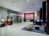 Modern hotel lobby with seating area, red and white chairs, a reception desk, and decorative red chandelier.