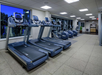A modern gym with a row of treadmills and ellipticals, large windows, and overhead lighting.