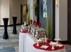 Buffet table set with chafing dishes, plates, and decorations in a conference room with cocktail tables and wall art.