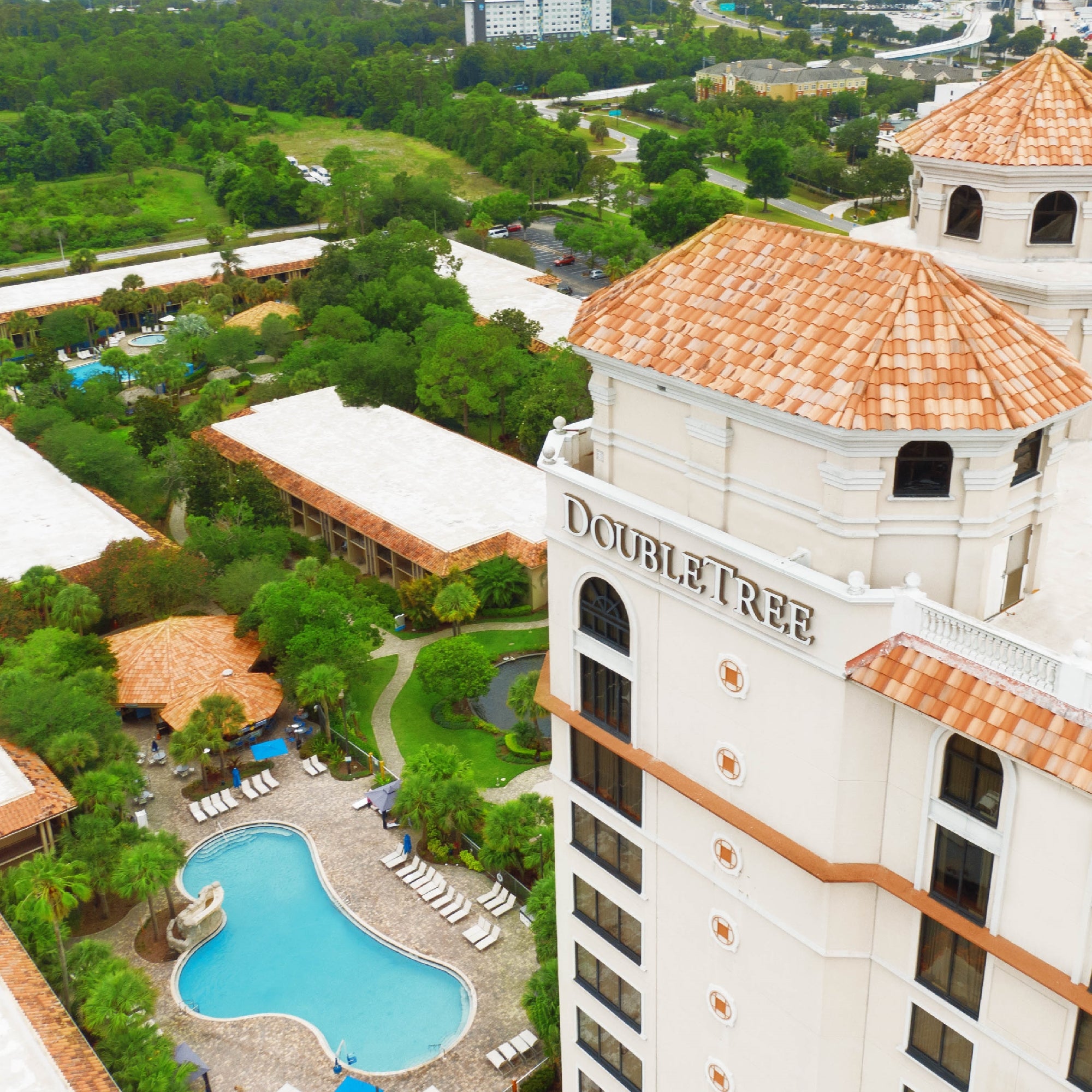 Aerial view of the DoubleTree hotel building with swimming pools, lounge chairs, and surrounding greenery.