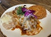 A plate with refried beans topped with cheese, enchiladas covered in melted cheese and sauce, garnished with cilantro and a flower, and a serving of Mexican rice.