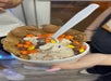 A hand holds a cup of ice cream topped with Reese’s Pieces and sprinkles, served in a bubble waffle with a white plastic spoon.