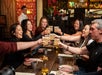 A group of people sitting at a restaurant table raise their drinks for a toast, smiling and enjoying each other's company.