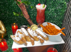 A plate of churros with dipping sauces and sweet potato fries next to a red cocktail, surrounded by candles and greenery.