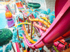 Colorful water slides intertwine in an indoor water park with palm decorations and a large pool area.