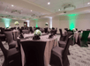 A large banquet area with gray cloth covered tables set for dinner with floral center pieces and black cloth covered chairs.