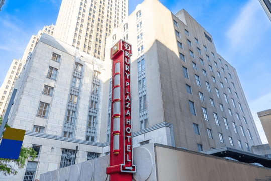 Looking up at the exterior of the Drury Plaza Hotel Pittsburgh Downtown with a red vertical neon sign in front.