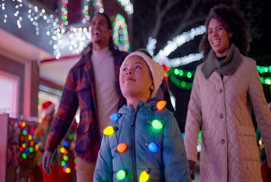 A family walks outside, enjoying colorful holiday lights.