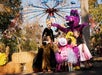 A group of young children in costumes gather around an adult in black and a person in a purple dragon costume at an outdoor amusement park.