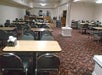 Empty dining area with several tables and chairs, floral carpet, and a small buffet station in the back.